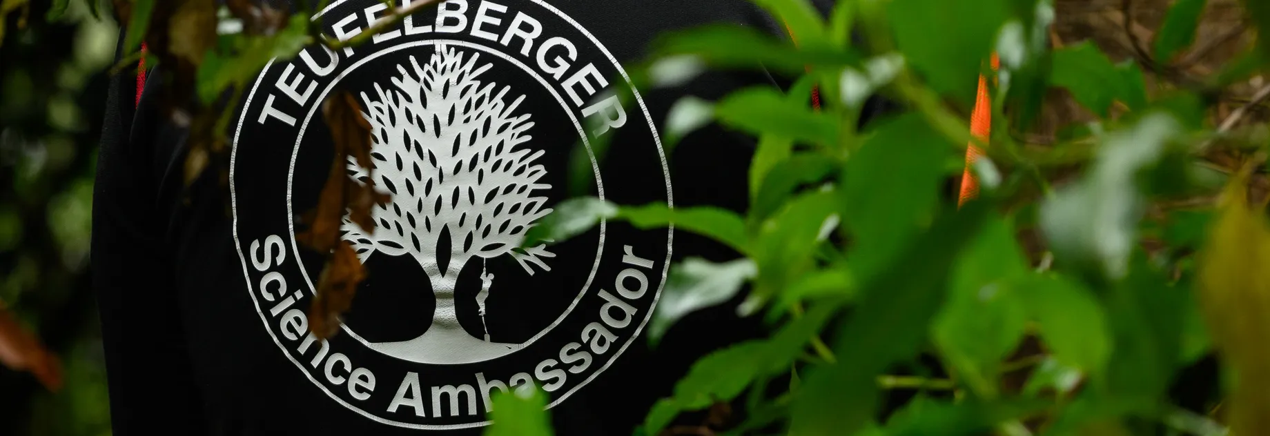 Moody shot of the Back of a Teufelberger Science Ambassador behind some green leaves