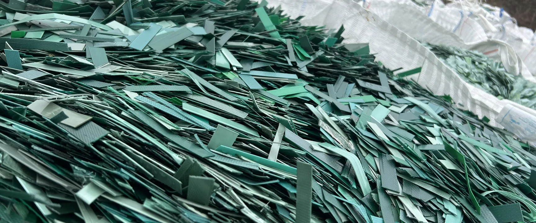 Close-up of green plastic strapping scraps piled up in a large white industrial bag, used for packaging and bundling.