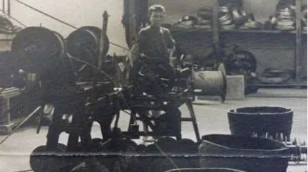 A person operating machinery in an industrial setting with large spools and baskets in the background.