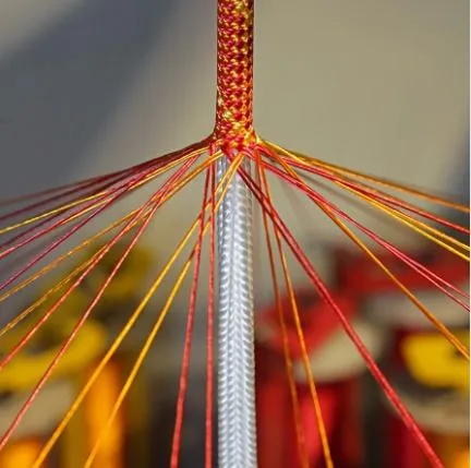 Close-up of colorful threads, in red, yellow, and orange, woven around a central rod, resembling a spider web pattern.