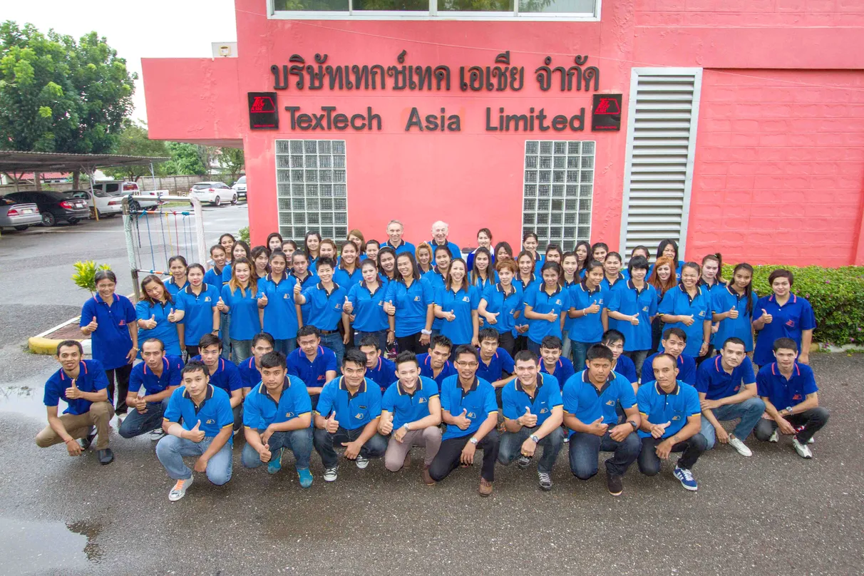Group of people wearing blue shirts posing in front of a building with "TexTech Asia Limited" signage.