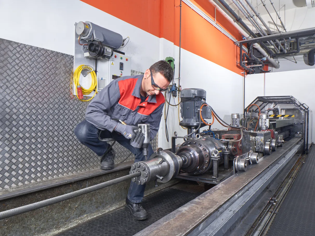 An employee is inspecting a steel wire rope on a tensile testing machine.