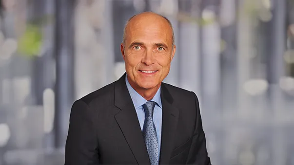 Smiling man in a suit with a blurred background.