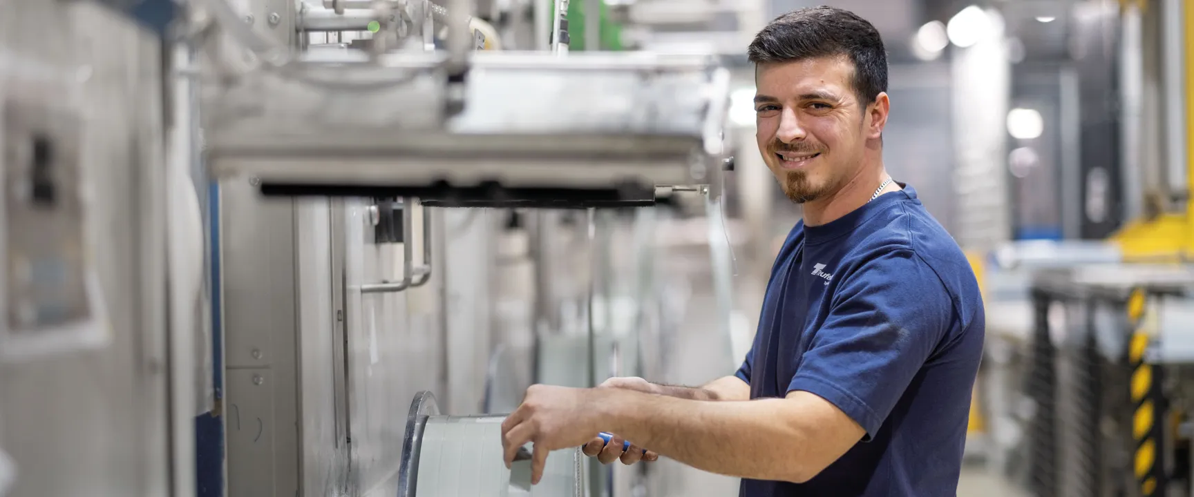 Worker operating machine with large spool system in industrial production environment at Teufelberger.