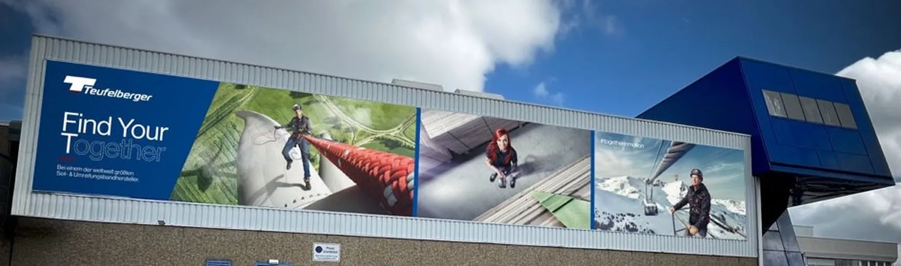 Large industrial building with blue accents, featuring outdoor sports-themed advertisements and the slogan "Find Your Together." Cloudy sky above.