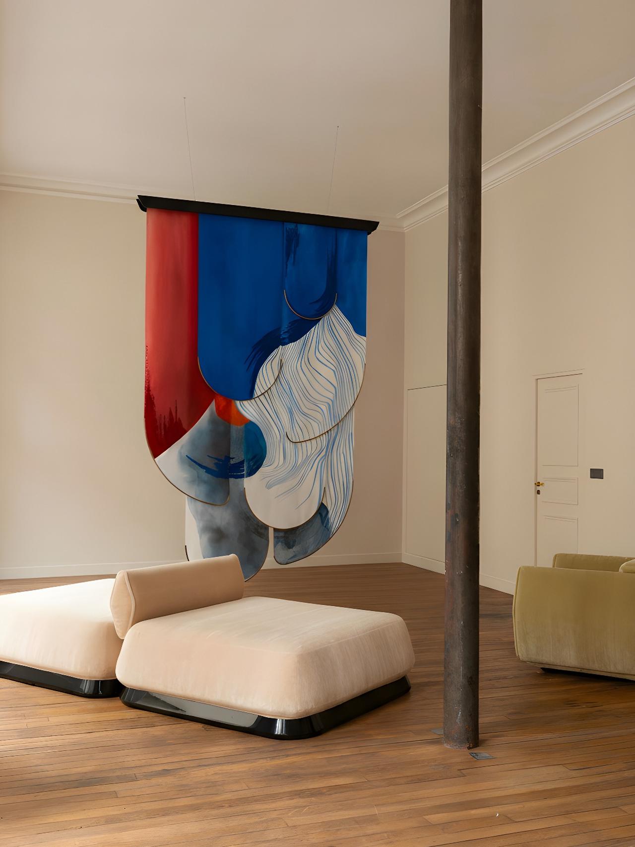 A modern room with two beige seating units, a vertical metal pole, and an abstract blue and red hanging artwork on a beige wall.