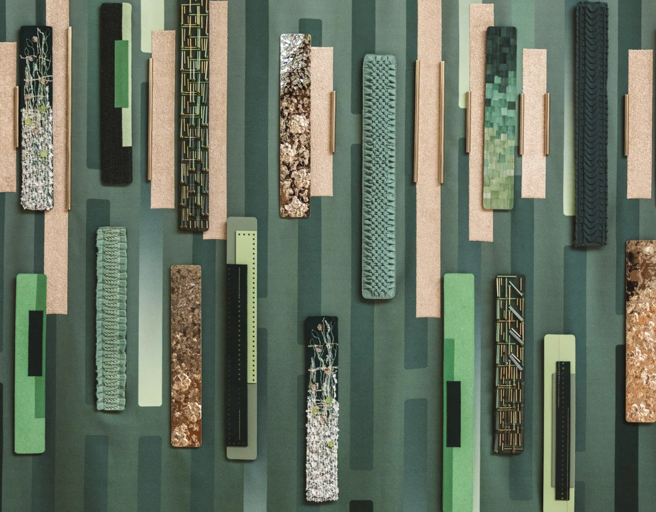 A textured wall art piece with vertical strips in green, brown, and beige tones, featuring varied patterns and materials like fabric and mosaic.
