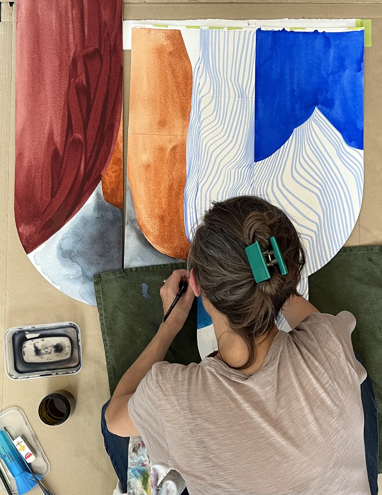 Person with a green hair clip painting abstract shapes on a large canvas with red, blue, and orange sections. Art supplies are nearby.