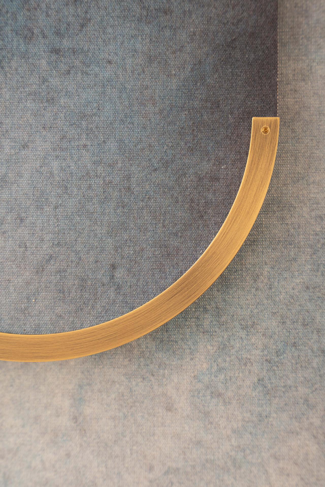 Close-up of a curved, brass metallic object against a textured blue-gray background, exhibiting a smooth finish and minimalist design.