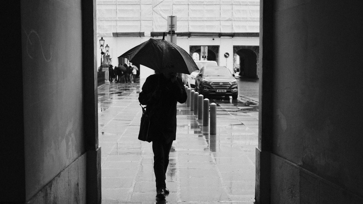 A man holding an umbrella walks in out of the rain