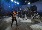 Costumed actress aims a bow in a snow-covered ruin set on Studio Ulster’s LED stage, with a large digital ogre projected on the curved screen behind her.