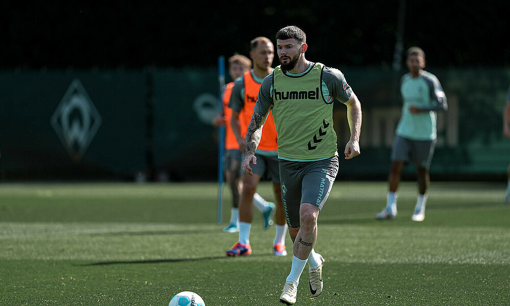 Oliver Burke beim Teamtraining mit einem Leibchen an am Ball.
