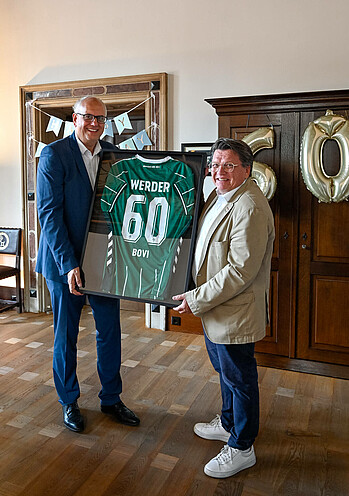 Hubertus Hess-Grunewald übergibt ein eingerahmtes Werder Trikot an Andreas Bovenschulte in der Senatskanzlei. 