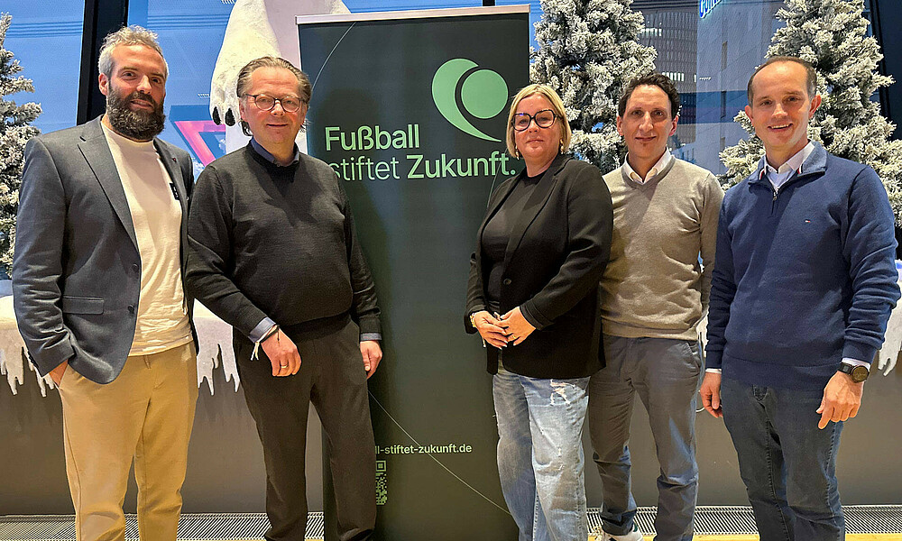 Henrik Oesau steht mit anderen Leuten zusammen vor einem Banner.