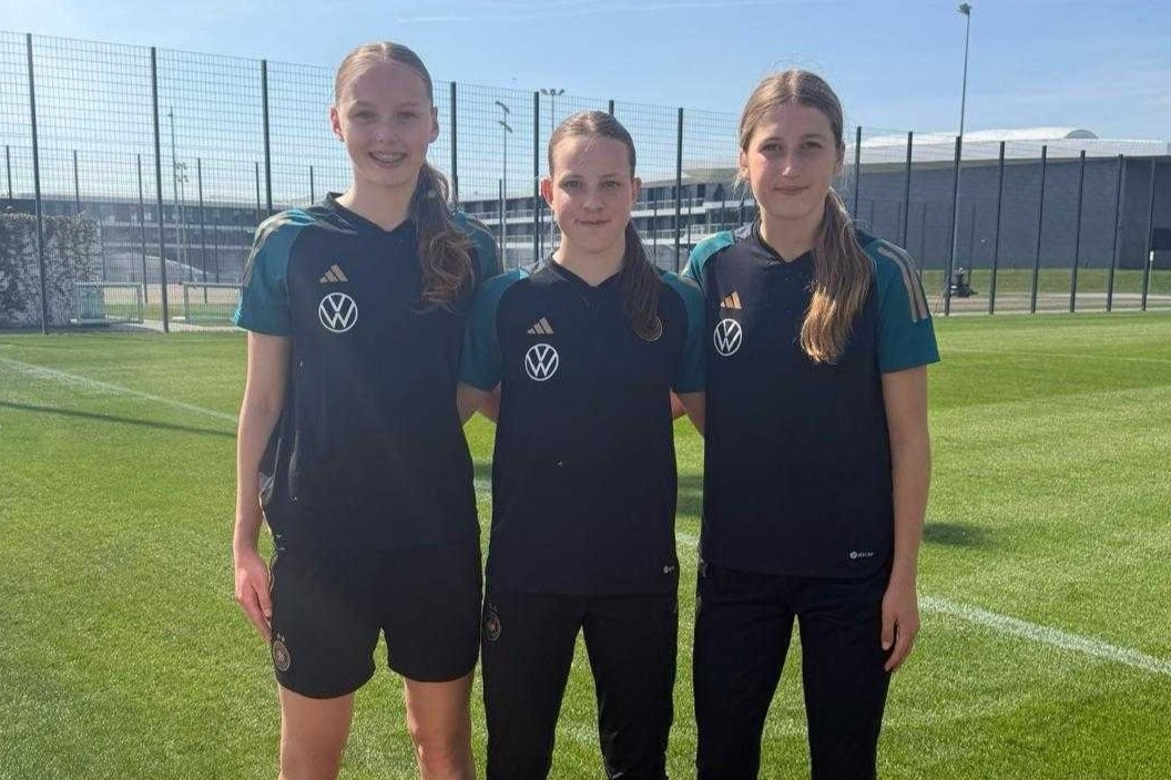 Drei Spielerinnen im DFB-Trainingsdress stehen Arm in Arm in Richtung Kamera