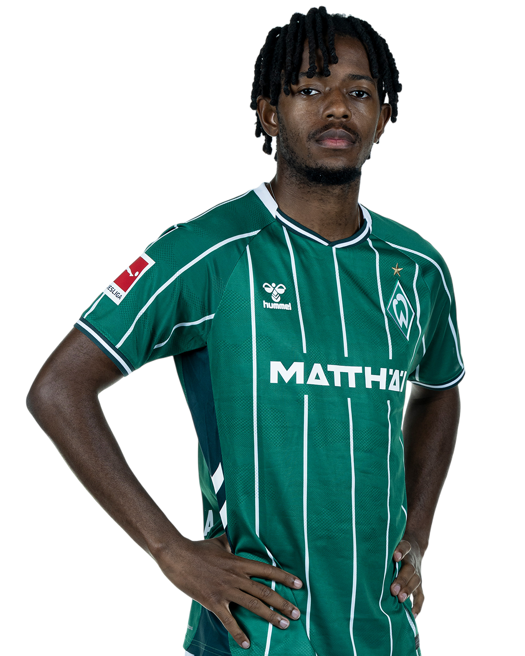 Samuel Mbangula in einem grün-weiß gestreiften Trikot mit der Aufschrift „MATTHÄI“ auf der Vorderseite steht mit den Händen in den Hüften da und schaut nach vorne.