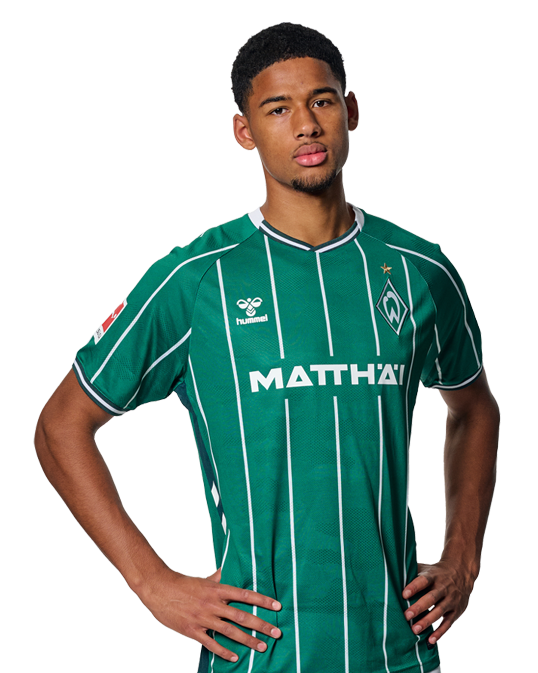 Salim Musah in einem grün-weiß gestreiften Trikot mit der Aufschrift „MATTHÄI“ auf der Vorderseite steht mit den Händen in den Hüften da und schaut nach vorne.
