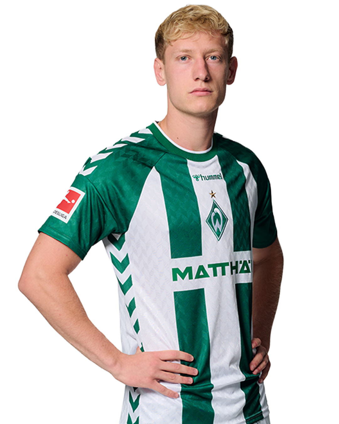 Ein Mann in einem grün-weiß gestreiften Fußballtrikot von Werder Bremen steht selbstbewusst mit den Händen in den Hüften vor einem einfarbigen Hintergrund.