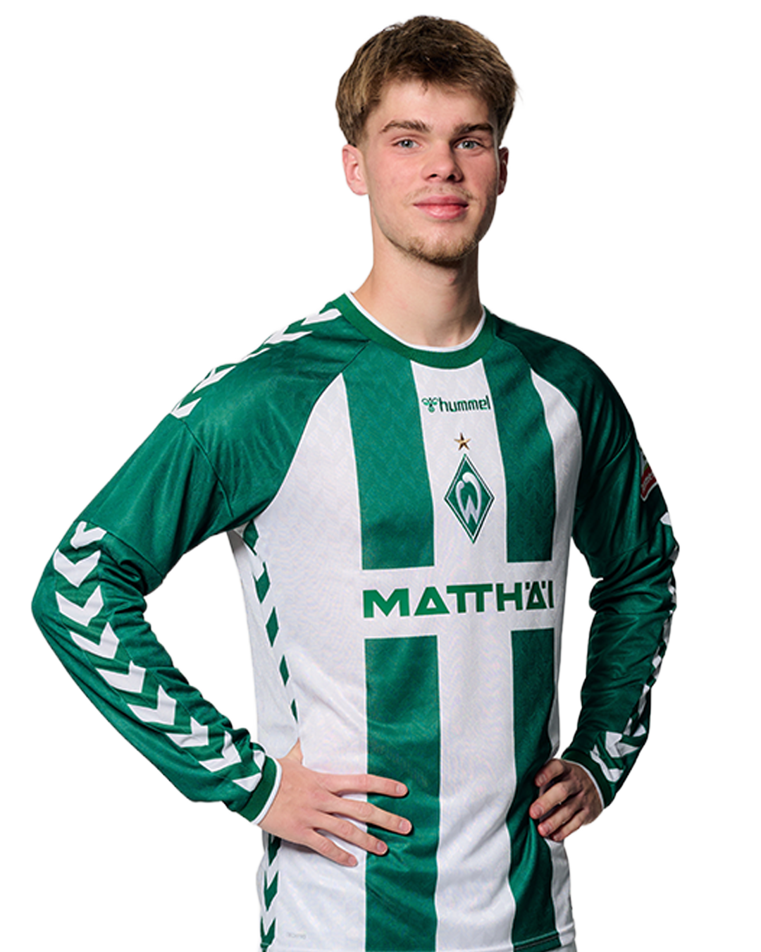 Ein Mann in einem grün-weiß gestreiften Fußballtrikot von Werder Bremen steht selbstbewusst mit den Händen in den Hüften vor einem einfarbigen Hintergrund.