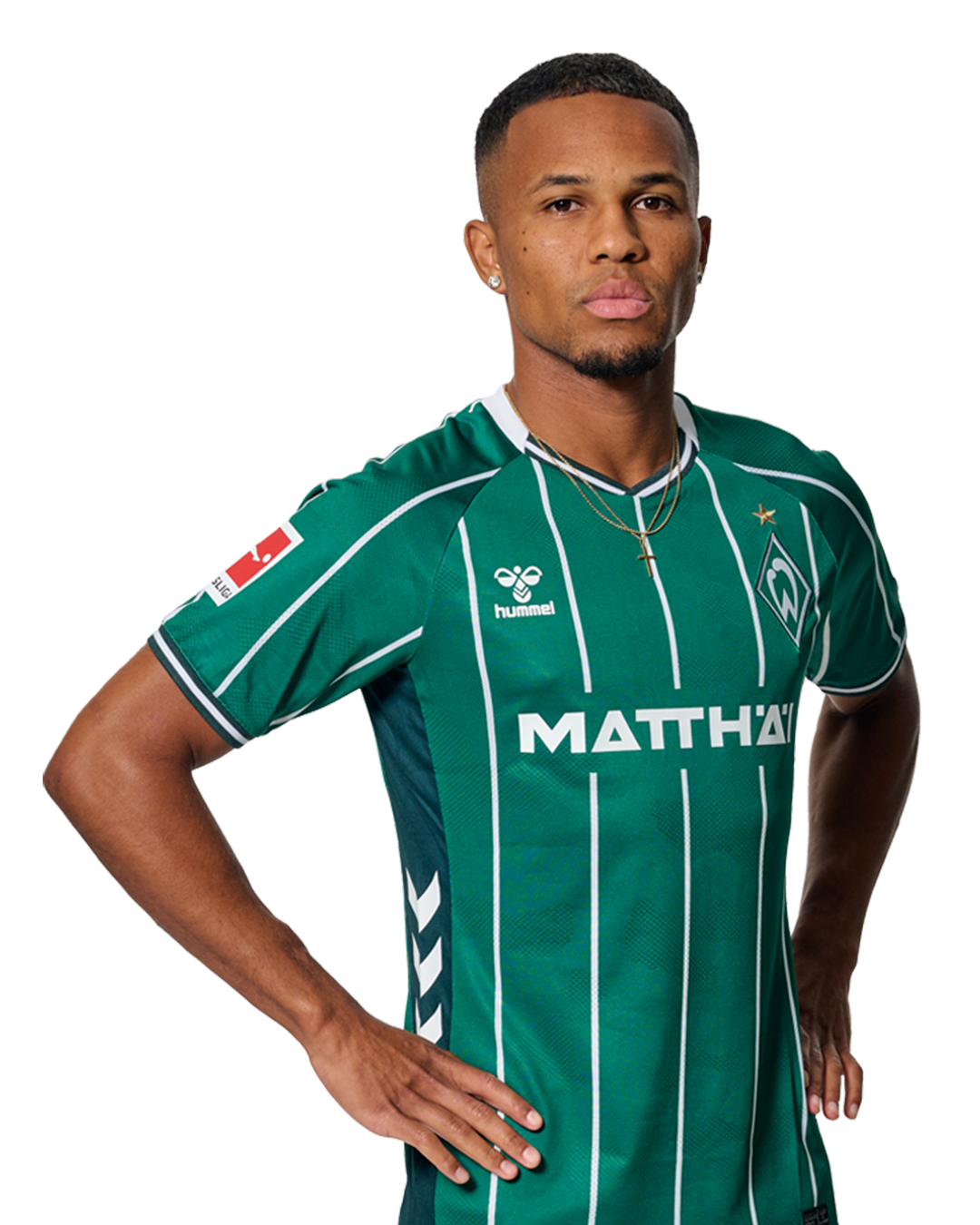 Felix Agu in einem grün-weiß gestreiften Trikot mit der Aufschrift „MATTHÄI“ auf der Vorderseite steht mit den Händen in den Hüften da und schaut nach vorne.