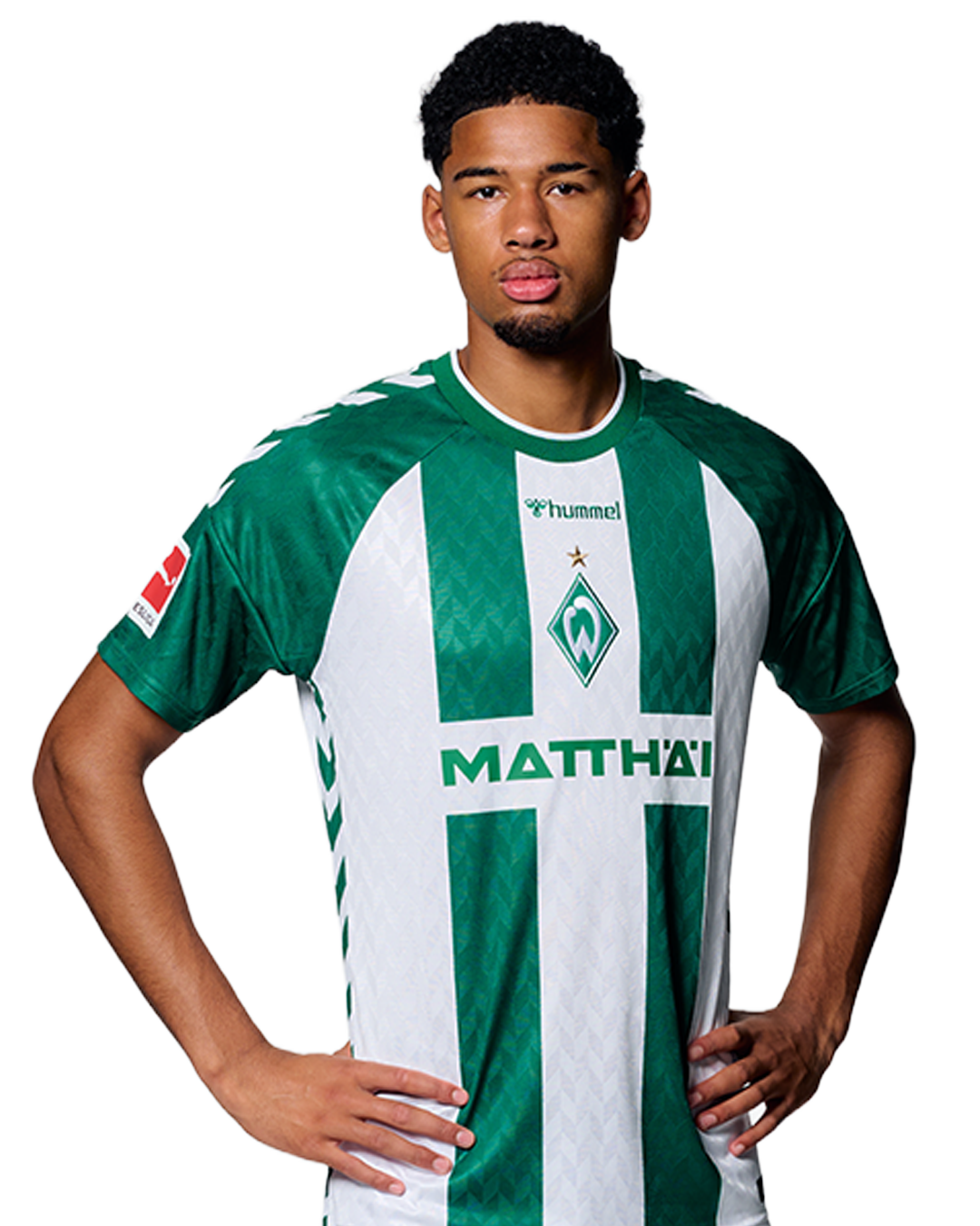Ein Mann in einem grün-weiß gestreiften Fußballtrikot von Werder Bremen steht selbstbewusst mit den Händen in den Hüften vor einem einfarbigen Hintergrund.