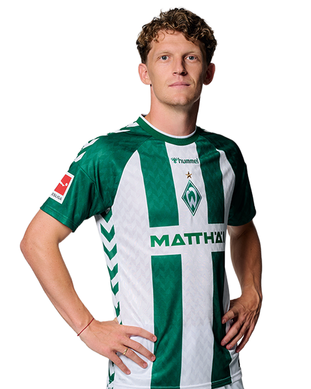 Ein Mann in einem grün-weiß gestreiften Fußballtrikot von Werder Bremen steht selbstbewusst mit den Händen in den Hüften vor einem einfarbigen Hintergrund.