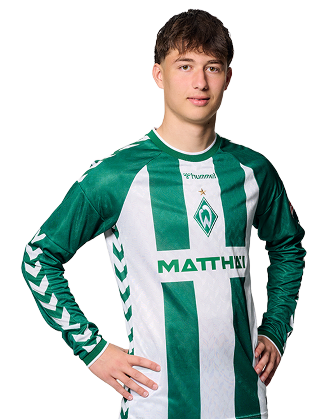Ein Mann in einem grün-weiß gestreiften Fußballtrikot von Werder Bremen steht selbstbewusst mit den Händen in den Hüften vor einem einfarbigen Hintergrund.