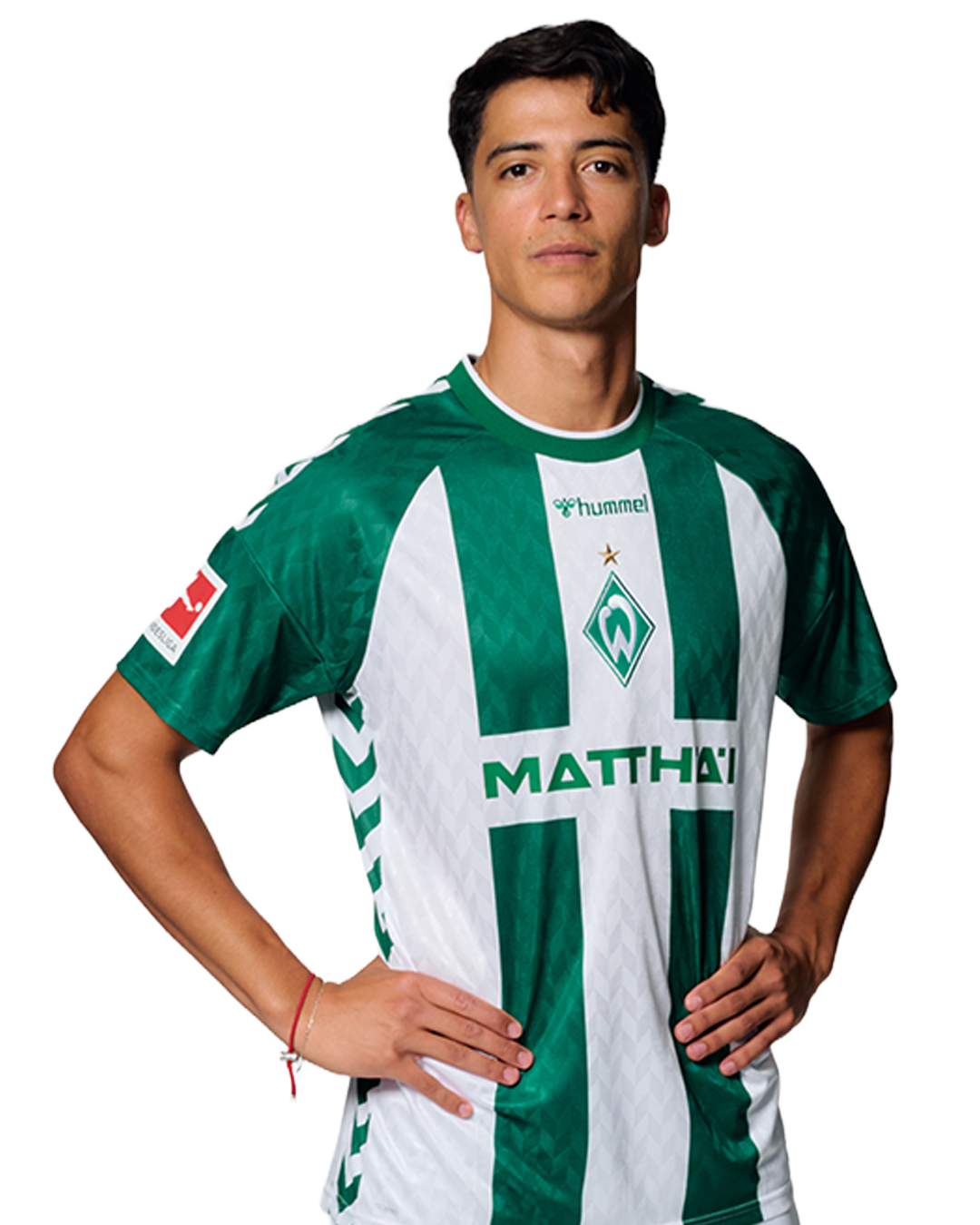 Ein Mann in einem grün-weiß gestreiften Fußballtrikot von Werder Bremen steht selbstbewusst mit den Händen in den Hüften vor einem einfarbigen Hintergrund.