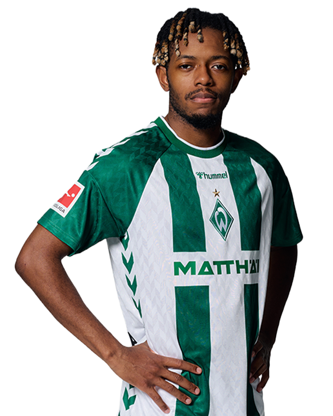 Ein Mann in einem grün-weiß gestreiften Fußballtrikot von Werder Bremen steht selbstbewusst mit den Händen in den Hüften vor einem einfarbigen Hintergrund.