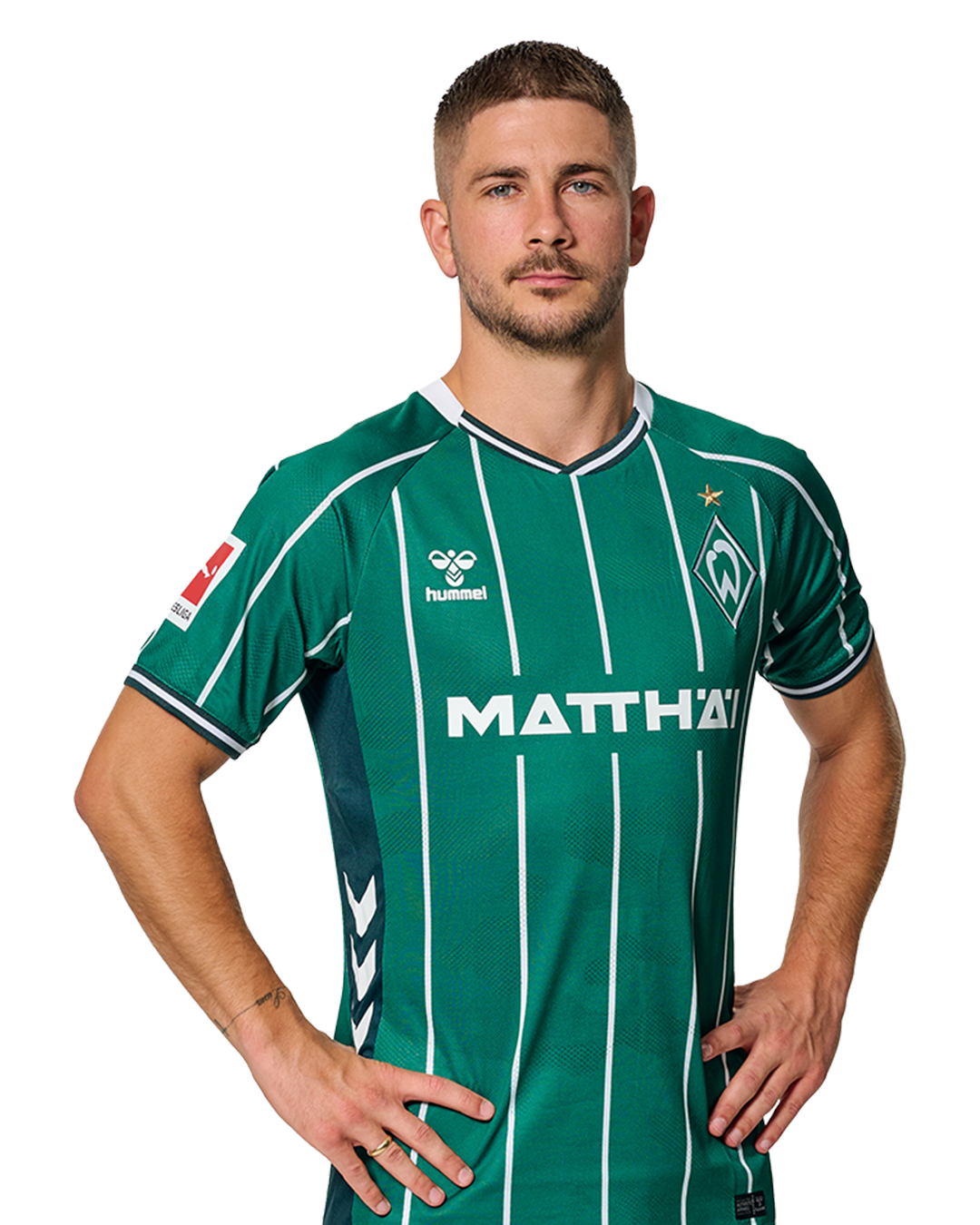 Romano Schmid in einem grün-weiß gestreiften Trikot mit der Aufschrift „MATTHÄI“ auf der Vorderseite steht mit den Händen in den Hüften da und schaut nach vorne.