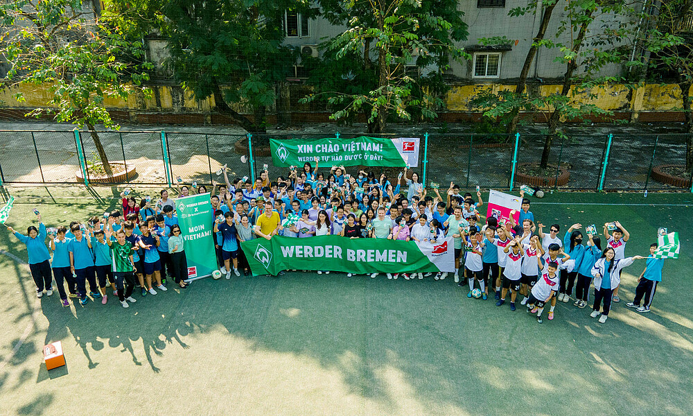 Viele Menschen stehen auf einem Fußballplatz zusammen. Sie freuen sich und halten ein Banner mit der Aufschrift Werder Bremen hoch.