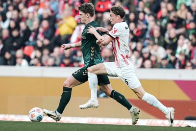 Jens Stage mit Ball am Fuß, im Hintergrund die Bayern-Kurve.