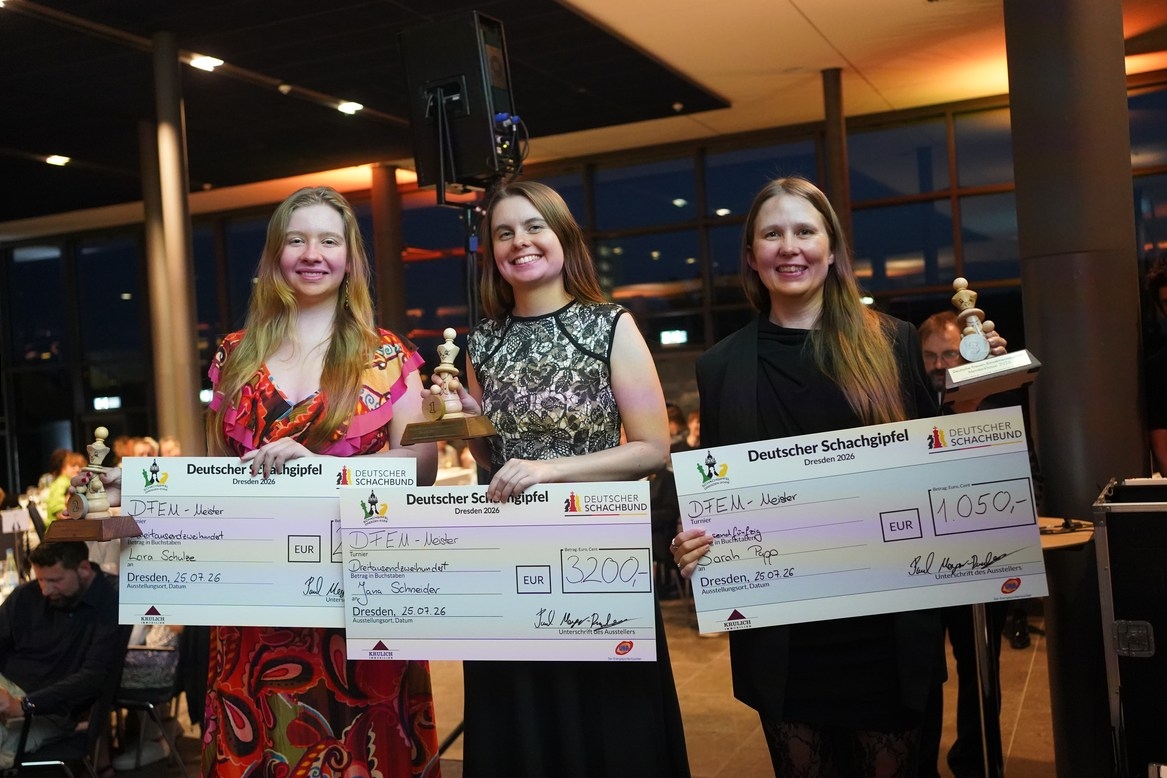 Three women holding large checks and trophies, smiling, standing in a well-lit event space.