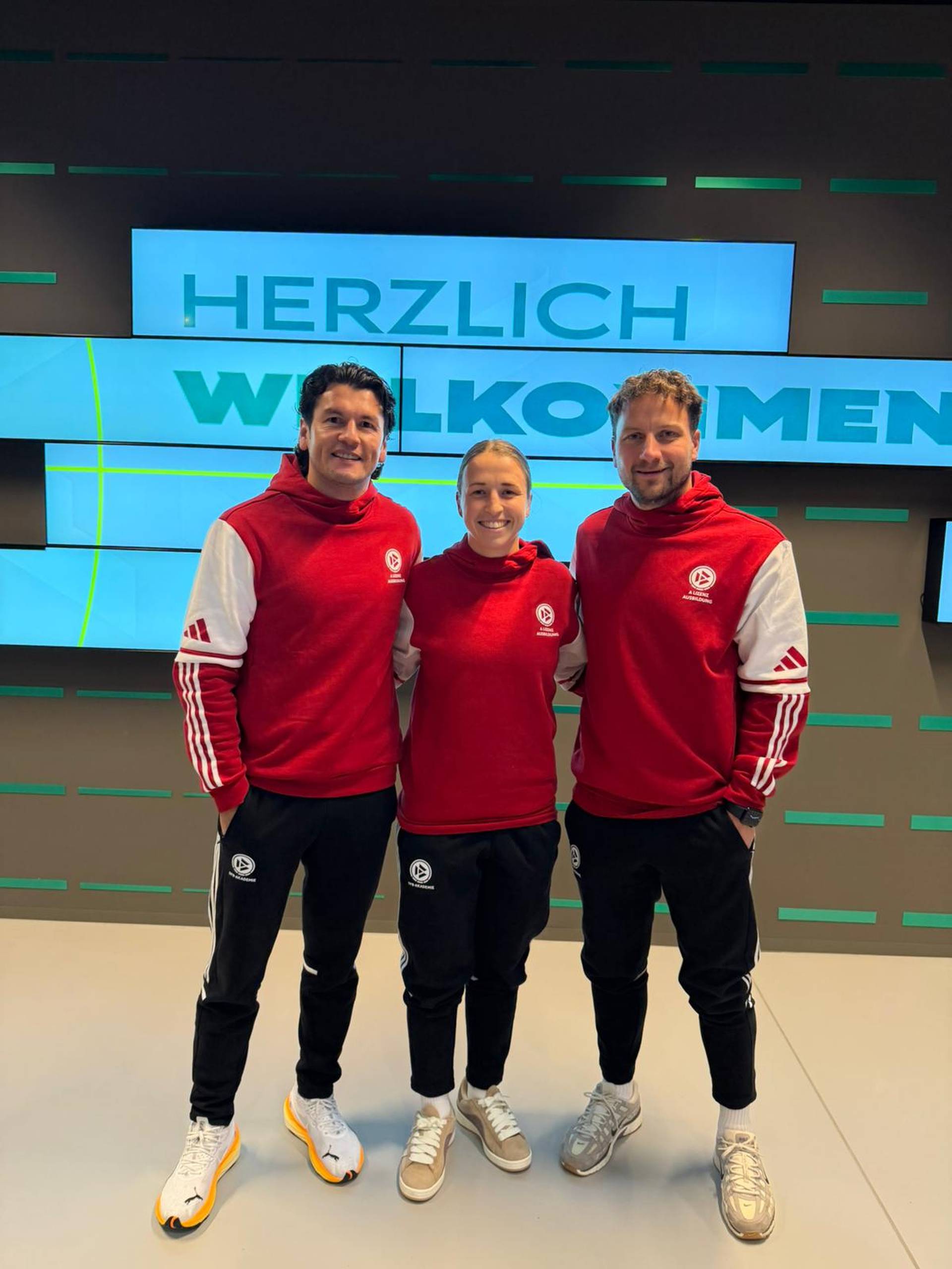 Nelson Valdez, Michaela Specht und Philipp Bargfrede stehen nebeneinander und lächeln. Alle tragen einen roten Pullover.