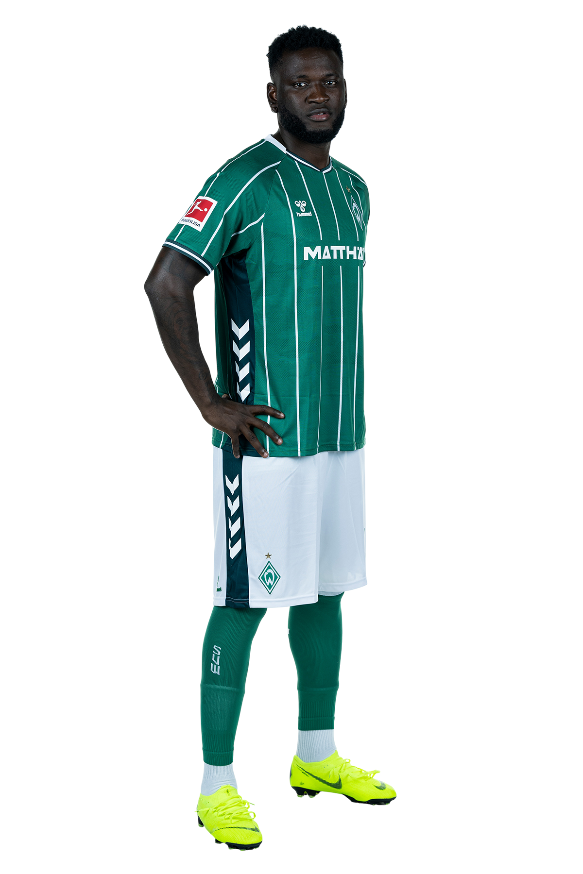 Victor Boniface in einem grün-weiß gestreiften Trikot mit der Aufschrift „MATTHÄI“ auf der Vorderseite steht mit den Händen in den Hüften da und schaut nach vorne.