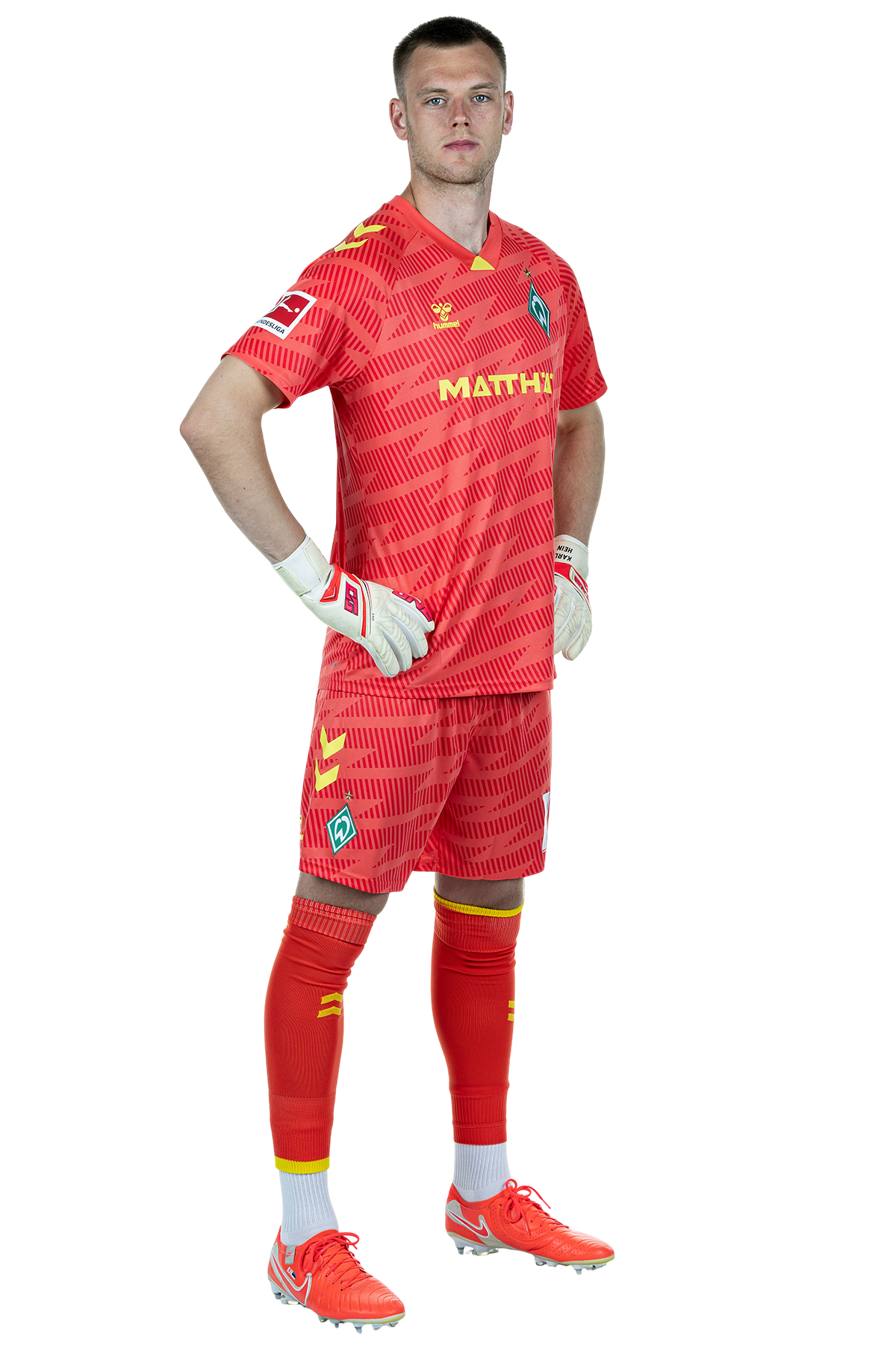 Karl Hein im rotem Trikot mit der Aufschrift "MATTHÄI" und Handschuhen, der selbstbewusst mit den Händen in den Hüften dasteht und nach vorne schaut.