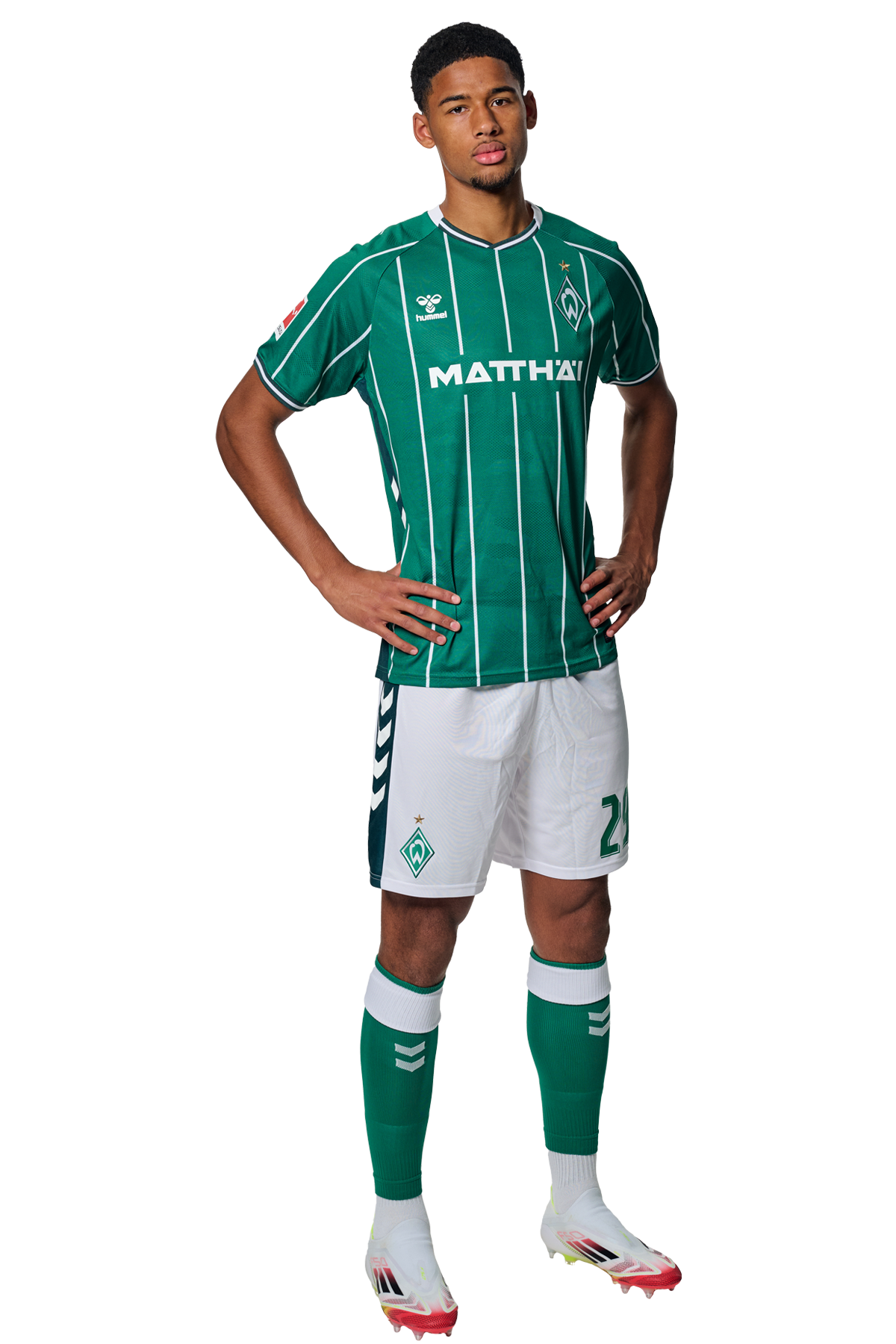 Salim Musah in einem grün-weiß gestreiften Trikot mit der Aufschrift „MATTHÄI“ auf der Vorderseite steht mit den Händen in den Hüften da und schaut nach vorne.
