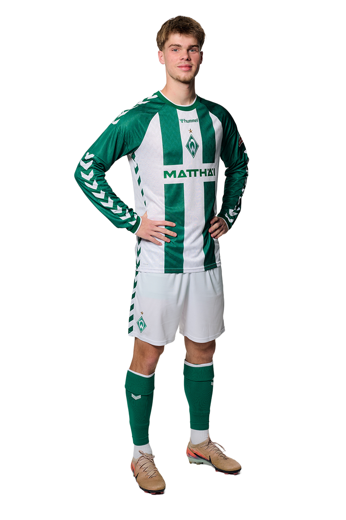 Ein Mann in einem grün-weiß gestreiften Fußballtrikot von Werder Bremen steht selbstbewusst mit den Händen in den Hüften vor einem einfarbigen Hintergrund.
