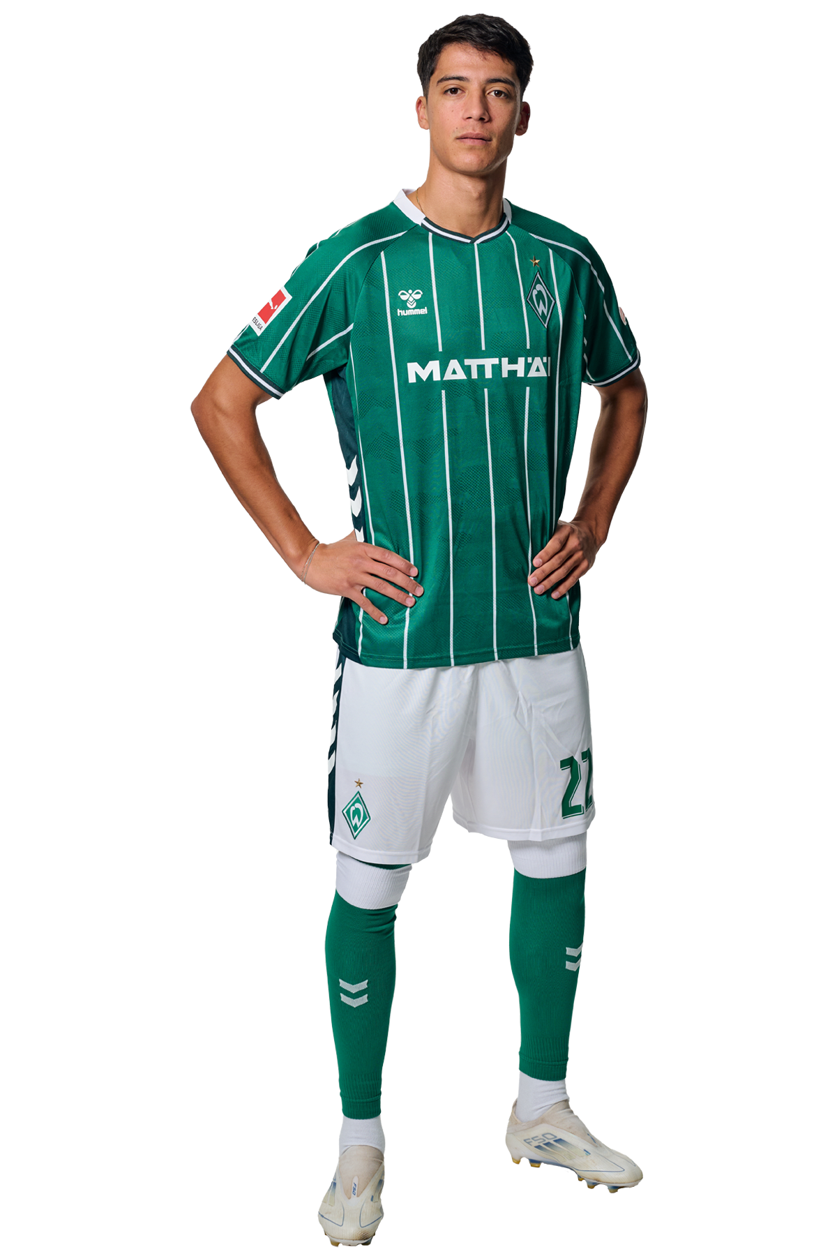 Julián Malatini in einem grün-weiß gestreiften Trikot mit der Aufschrift „MATTHÄI“ auf der Vorderseite steht mit den Händen in den Hüften da und schaut nach vorne.