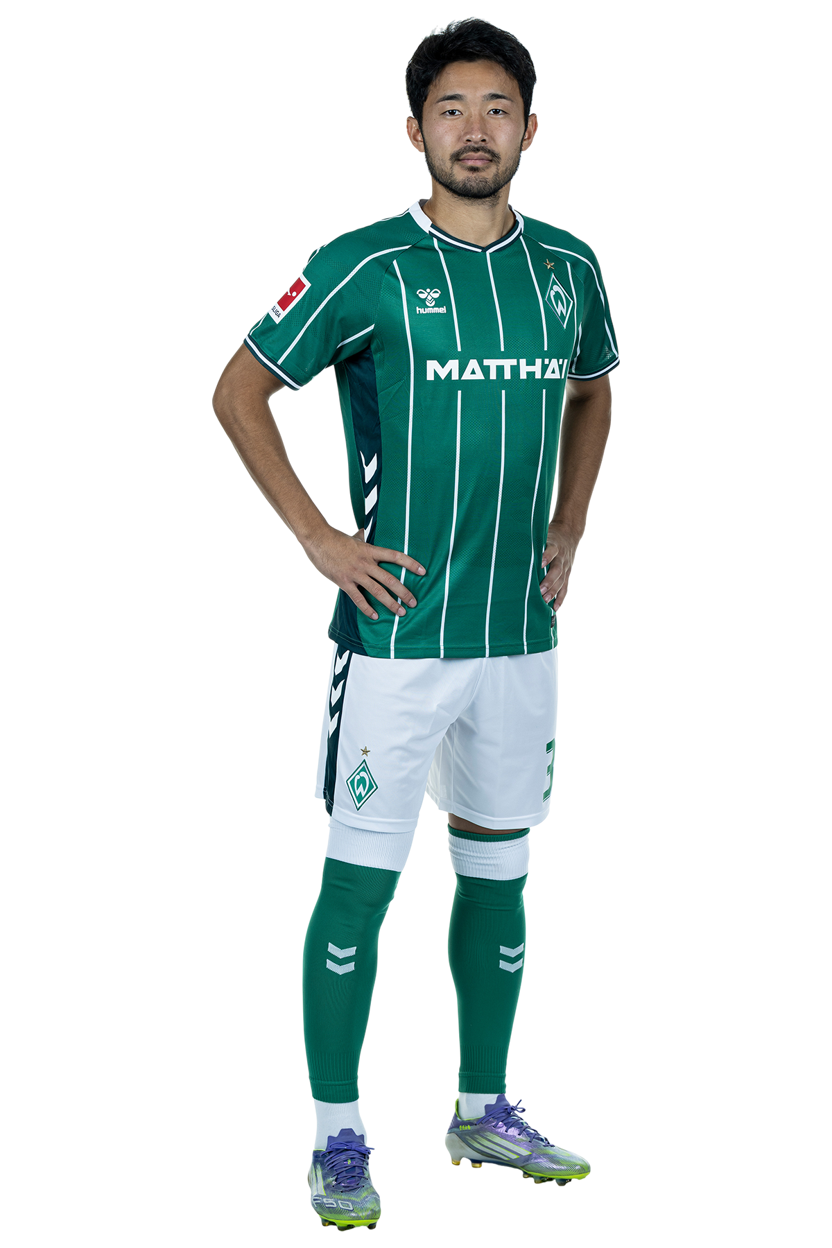 Yukinari Sugawara in einem grün-weiß gestreiften Trikot mit der Aufschrift „MATTHÄI“ auf der Vorderseite steht mit den Händen in den Hüften da und schaut nach vorne.