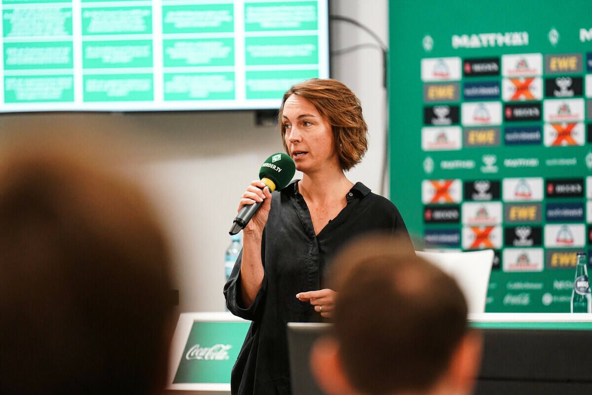 Anne-Kathrin Laufmann hat ein Mikrofon in der Hand und spricht vor Menschen im PK-Raum des Weserstadions.