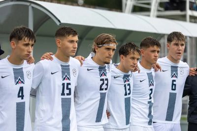 Sechs Fußballspieler in weißen Trikots stehen in einer Reihe, die Arme umeinander gelegt, konzentriert und bereit für das Spiel. In der Mitte steht Noah Weissbach. Er trägt die Nummer 23.