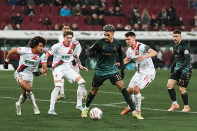 Justin Njinmah mit Ball am Fuß umzingelt von mehreren Augsburgern.