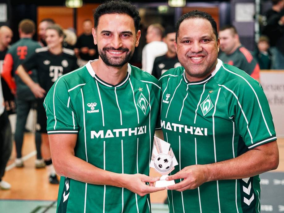 Mehmet Ekici und Ailton lächeln mit einer Trophäe in die Kamera.