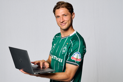 Niklas Stark hält einen Laptop in der Hand. Er steht vor einem weißen Hintergrund.