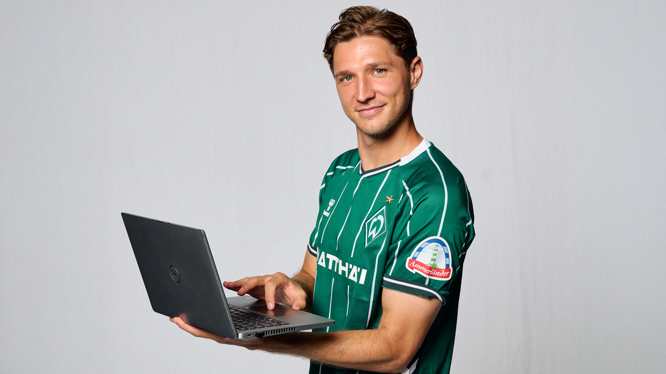 Niklas Stark hält einen Laptop in der Hand. Er steht vor einem weißen Hintergrund.