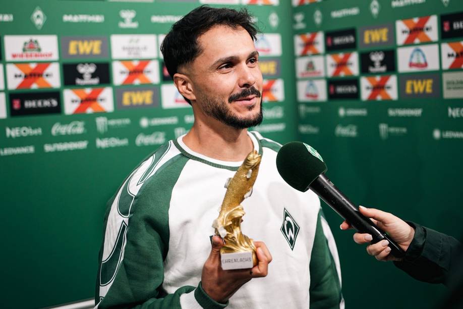 Leonardo Bittencourt stands in the mixed zone holding a trophy of a golden salmon.