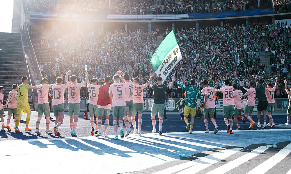 Die Mannschaft steht vor der Auswärtskurve in Berlin. Alle reißen die Arme hoch.