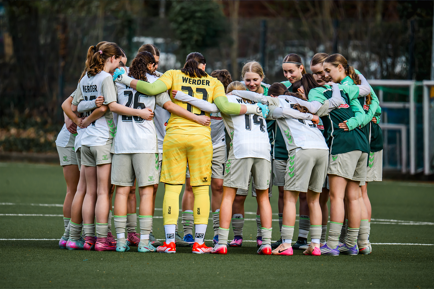 Die U17-Juniorinnen stehen im weißen Auswärtstrikot auf dem Platz und bilden einen Mannschaftskreis.
