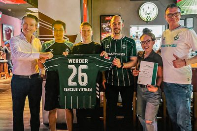 Sechs Personen stehen in einer Bar und halten lächelnd ein Werder 26 Vietnam Trikot hoch,